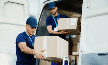young-courier-his-colleague-unloading-cardboard-boxes-from-delivery-van 1
